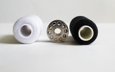 Sewing supplies. Reels with black and white threads, bobbin with black thread on a gray background
