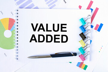 Notepad with text Value Added, paper clips, blue pen on financial diagrams