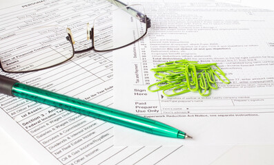 A green pen sits on the financial tables with green paper clips and eyeglasses