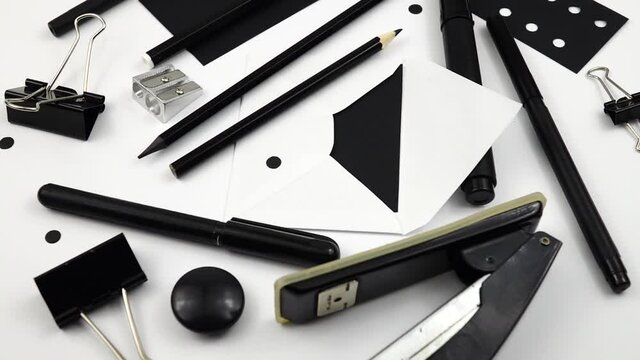 Various stationery in black are laid out on white table, slow motion