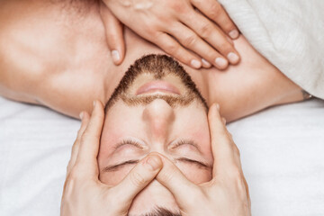 Fototapeta na wymiar Top view of relaxing young caucasian man enjoying head massage by two masseurs