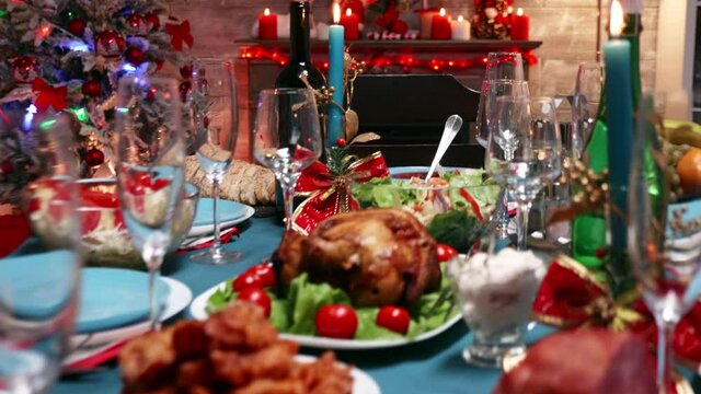 Table with delicious food ready for christmas feast of a big family. Fireplace in the background. Xmas celebration in decorated room full of globe decorations and christmas tree with fireplace, big