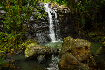 Waterfall landscape. Beautiful hidden waterfall in tropical rainforest. Foreground with big stones. Fast shutter speed. Sing Sing Angin waterfall, Bali, Indonesia