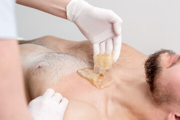 Epilation chest of young male with liquid wax paste by hands of female cosmetologist in beauty salon
