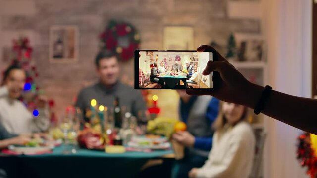 Girl taking a family portrait with her phones while celebrating christmas. Traditional festive christmas dinner in multigenerational family. Enjoying xmas meal feast in decorated room. Big family