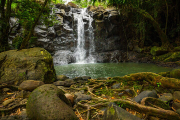 Waterfall landscape. Beautiful hidden waterfall in tropical rainforest. Foreground with big stones. Fast shutter speed. Sing Sing Angin waterfall, Bali, Indonesia