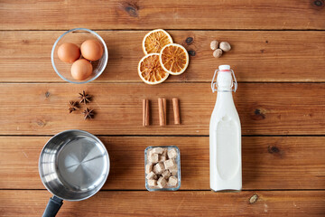 cooking, christmas and seasonal drinks concept - ingredients for eggnog, pot on wooden background