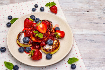 Cottage cheese pancakes with fresh berries and strawberry sauce. Healthy breakfast concept on wooden background