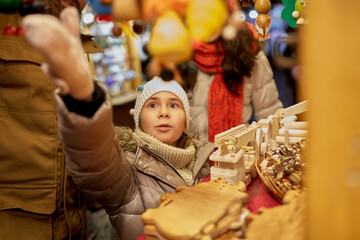 winter holidays and celebration concept - happy girl with family choosing souvenirs at christmas market on town hall square in tallinn, estonia