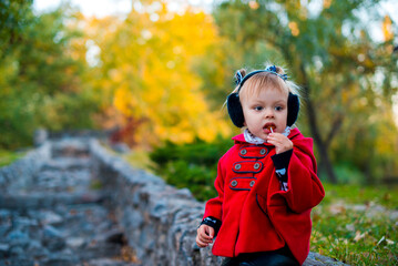 Portrait of a cute little girl in the fall. Fashionable baby in a red coat for a walk. Beautiful...