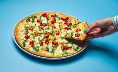 Hand of woman take a slice of delicious Italian pizza with tomatoes cherry, cheese mozzarella and sauce pesto on blue table or background. Lunch break concept.