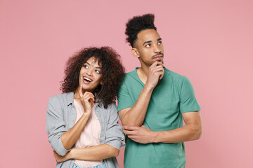 Pensive funny young african american couple friends guy girl in gray green casual clothes posing put hands prop up on chins looking up isolated on pastel pink color wall background studio portrait.