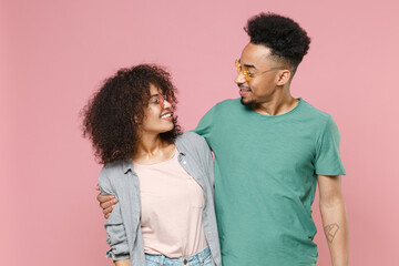Smiling young african american couple two friends guy girl in gray green casual clothes eyeglasses posing hugging looking at each other isolated on pastel pink color wall background studio portrait.