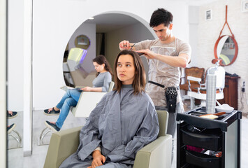 Young cheerful smiling man hairdresser working with female client in hairdressing salon.