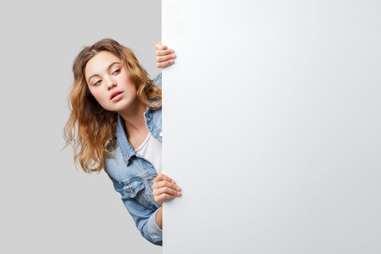Young woman peeking out from behind a white wall