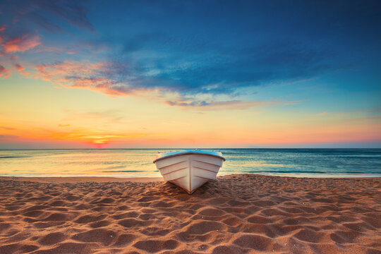 Tropical Seascape with a boat on sandy beach at cloudy sunrise or sunset