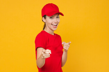 Fototapeta na wymiar Delivery employee woman in red cap blank t-shirt uniform workwear work courier in service during quarantine coronavirus covid-19 virus, posing look camera isolated on yellow background studio portrait