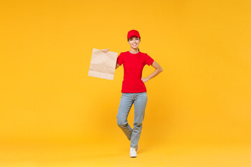 Full length body delivery employee woman in red cap blank t-shirt uniform work courier service in quarantine coronavirus covid-19 hold craft paper takeaway bag mockup isolated on yellow background.