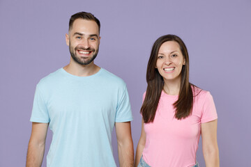 Fototapeta premium Smiling cheerful funny beautiful young couple two friends man woman 20s wearing blue pink empty blank design t-shirts stand looking camera isolated on pastel violet color background studio portrait.