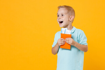 Little male traveler tourist kid boy 5-6 years old in blue t-shirt polo hold passport flight tickets isolated on yellow background child studio portrait. Passenger traveling abroad on weekends getaway