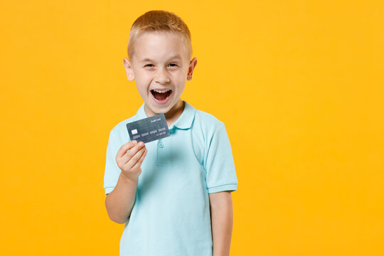 Excited Happy Little Fun Male Kid Boy 5-6 Years Old Wearing Stylish Blue Turquoise T-shirt Polo Hold In Hand Mockups Of Credit Bank Card Isolated On Yellow Color Wall Background Child Studio Portrait.