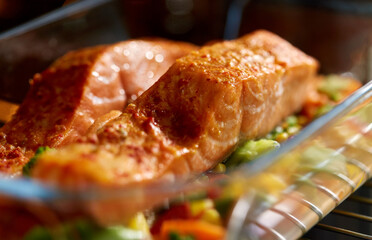 food, eating and culinary concept - salmon fish with vegetables cooking in baking dish in oven at...