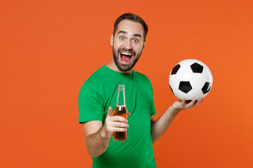 Excited young man football fan in green t-shirt cheer up support favorite team with soccer ball hold beer bottle pointing finger on camera isolated on orange background. People sport leisure concept.