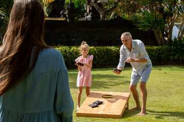 Happy family playing cornhole game outdoor on sunny summer day. Parents and children playing bean bag toss - 376643223