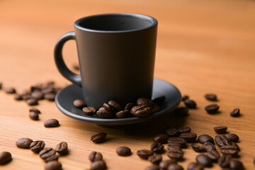 A grey cup of coffee on a wooden table with fresh coffee beans around with against a dark background