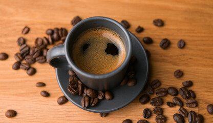 A grey cup of coffee on a wooden table with fresh coffee beans around with against a dark background