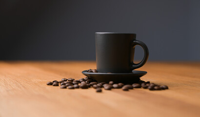 A grey cup of coffee on a wooden table with fresh coffee beans around with against a dark background