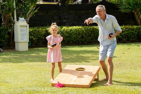 Happy family playing cornhole game outdoor on sunny summer day. Parents and children playing bean bag toss