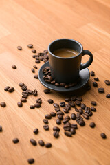 A grey cup of coffee on a wooden table with fresh coffee beans around with against a dark background