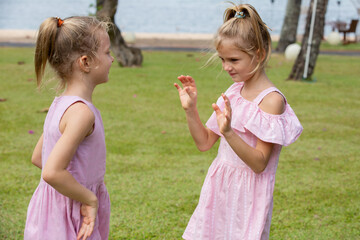 Two girls playing hand clapping game outdoors by the sea. Sisters having fun together outside on summer day