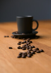 A grey cup of coffee on a wooden table with fresh coffee beans around with against a dark background