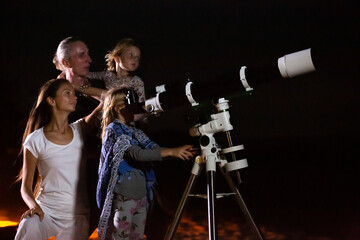 Happy family looking at moon and stars through a telescope at beautiful night sky. Parents and two...