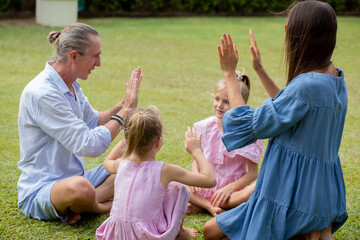 Family playing hand clapping game outdoors by the sea. Parents having fun together with children outside on summer day