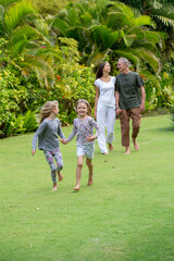 Fototapeta premium Young happy family walking in tropical park or gaden with palm trees. Two cute little sisters running in front of parents. Summer exotic vacation