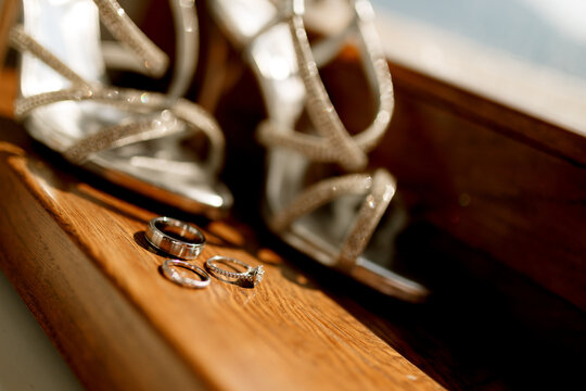 Wedding rings and an engagement ring on a wooden texture with women's wedding sandals on a blurred background.
