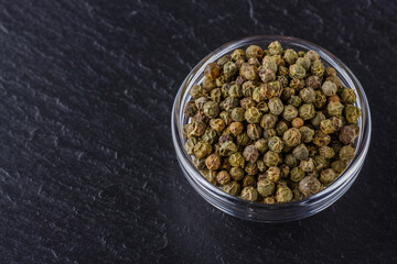 green peppercorns on dark slate stone background