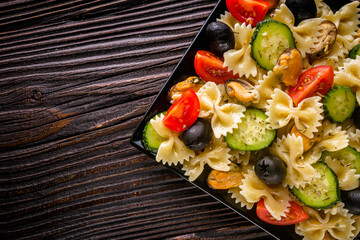 Delicious pasta salad with tomato cucumber and olives on wooden rustic background