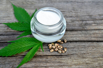 Cannabis cream in a jar with marijuana leaf and seeds on wooden background.CBD cosmetics,hemp extract,
herbal organic medicine, alternative or naturopathy concept.Selective focus.