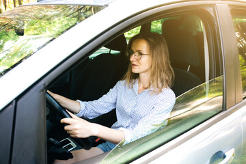 Woman in glasses  is driving a car. Girl behind the wheel.