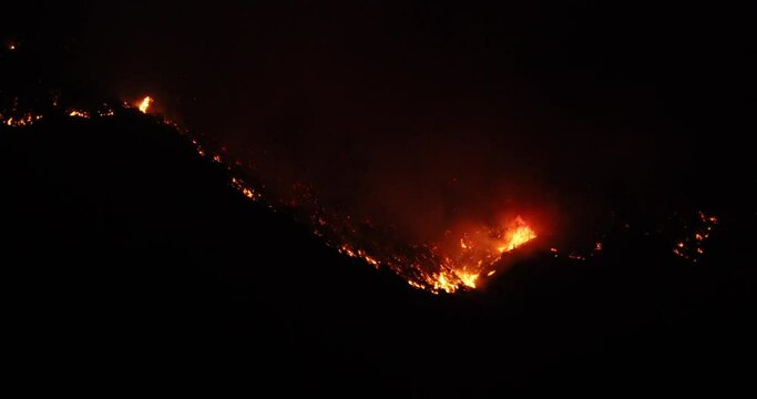 Dark night mountain wild forest fire blaze. Intense man caused wild and forest fire destroyed a mountain side and valley. Fire fighting crew on the ground supported by aircraft and helicopters.