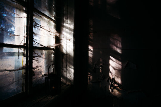 Eerie atmosphere in an abandoned building with huge windows and spider webs and one lamp. Halloween themed image. 