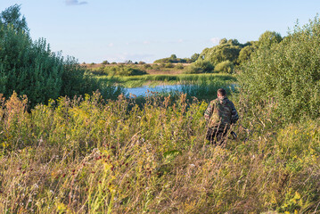 Hunting season concept. One hunter going to the pond on sunny autumn day before sunset