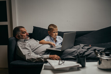 grandfather and his grandson relaxing on sofa at home using laptop computer