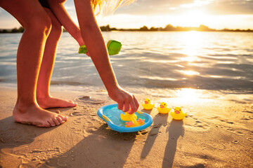 Side crop view of unrecognizable caucasian girl playing with rubber yellow ducks in small blue pool, standing on beach sand. Incognito kid having fun, enjoying holidays at seashore, summer sunset.