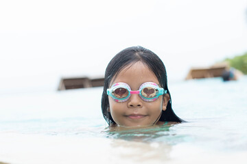 smiling cute little beautiful girl swims with goggles in outdoor swimming pool.