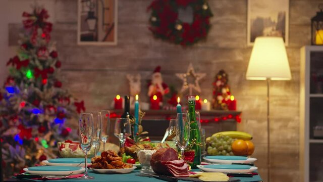 Glasses for champagne on christmas table with delicious traditional food. Xmas celebration in decorated room full of globe decorations and christmas tree with fireplace, big festive dinner meal for